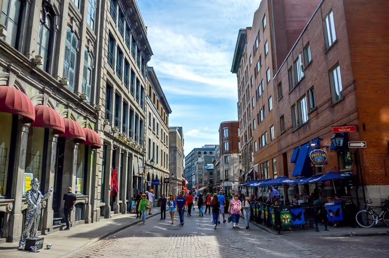Une rue animée du Vieux-Montréal, avec des bâtiments en pierre, des terrasses et des piétons.