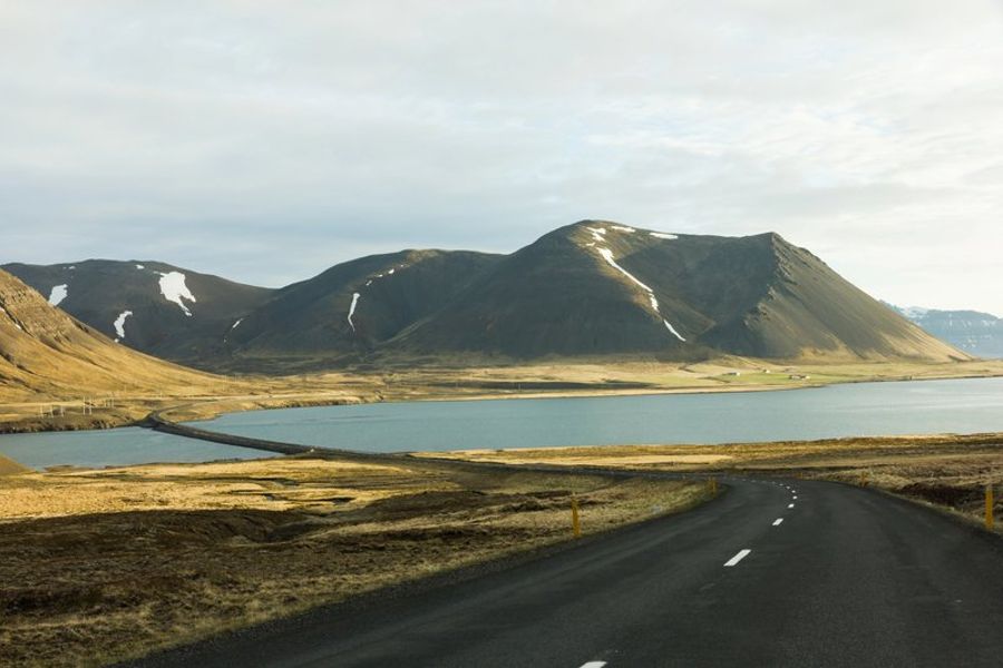 Route de la Ring Road longeant un fjord avec des montagnes partiellement enneigées en Islande