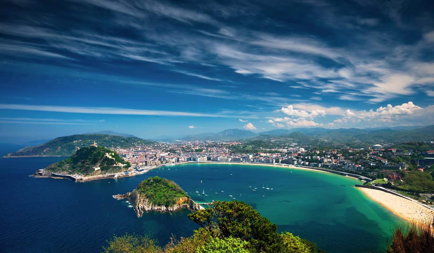 Vue panoramique de San Sebastián avec la baie de la Concha, l'île de Santa Clara, et les montagnes en arrière-plan.
