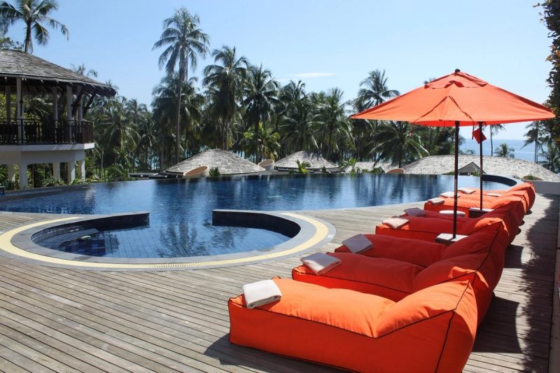 Piscine à débordement entourée de palmiers avec transats et parasols, offrant une vue paradisiaque sur une destination tropicale.