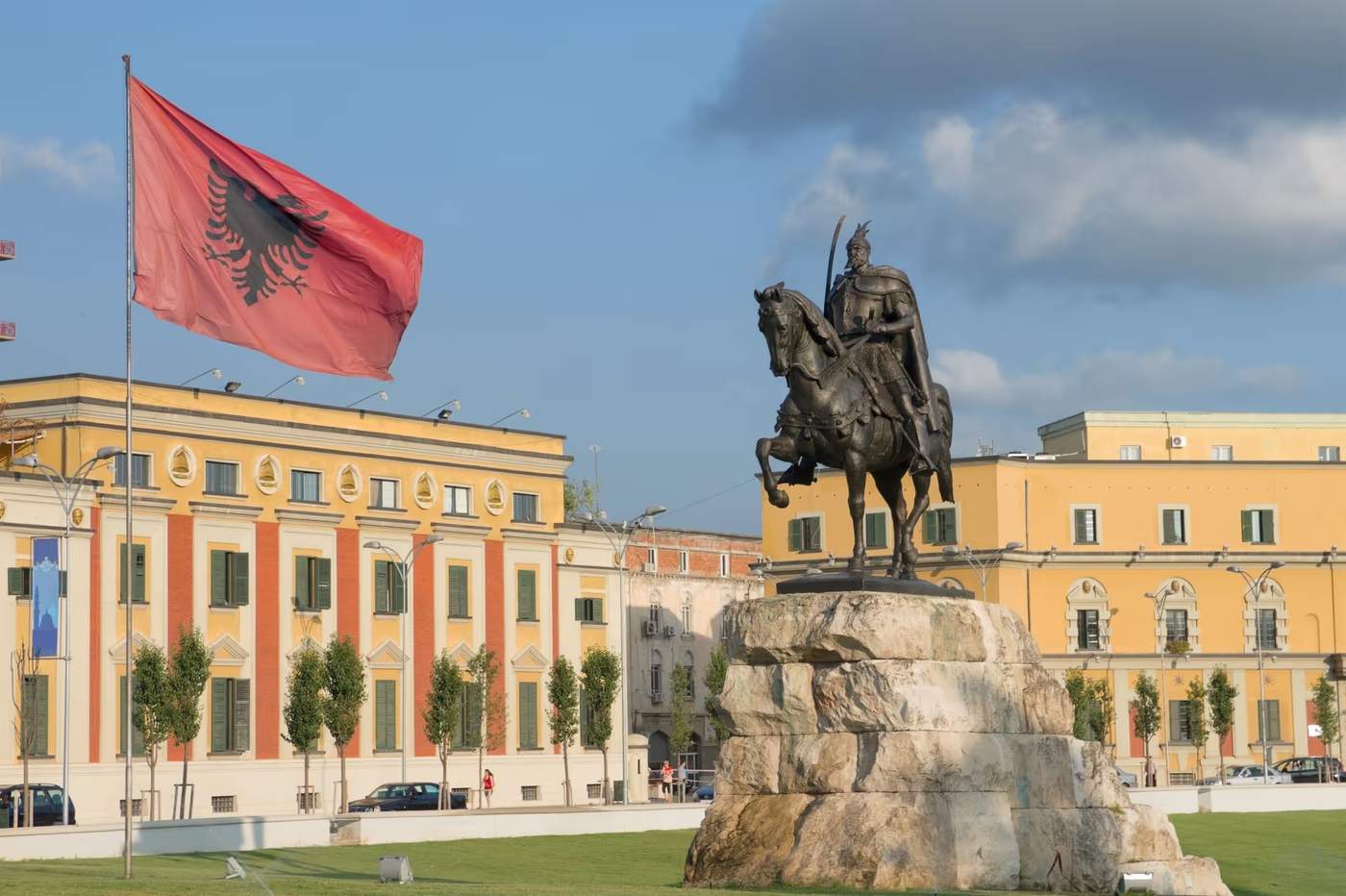 Statue de Skanderbeg et drapeau albanais sur la place Skanderbeg à Tirana, sous un ciel dégagé.
