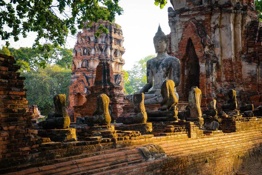 Statue de Bouddha en pierre entourée de ruines anciennes et de briques rouges à Ayutthaya.