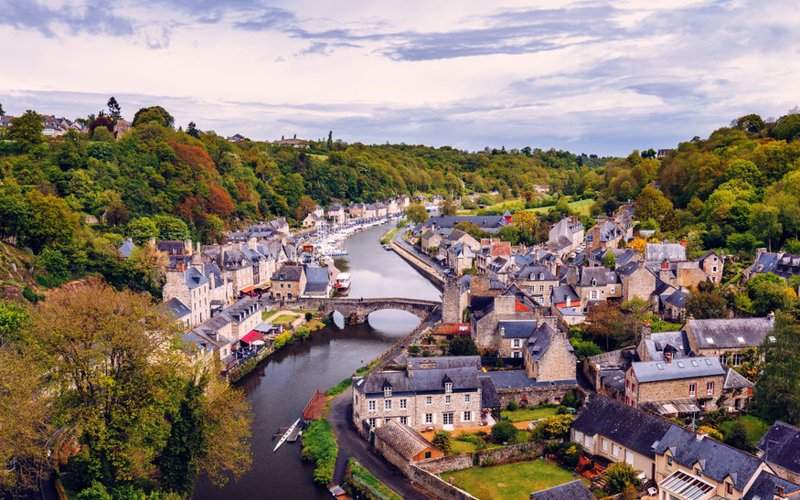 Vue pittoresque d'une ville en Bretagne avec une rivière traversant des maisons traditionnelles et un pont en pierre.