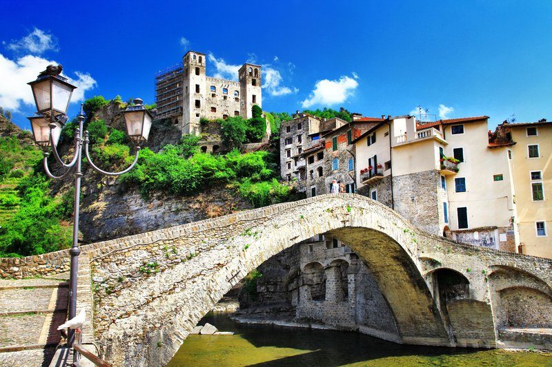 Le pont médiéval emblématique de Dolceaqua, surplombant une rivière, avec en arrière-plan les ruines d’un château et des maisons colorées.