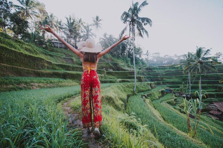 Femme explorant les rizières en terrasses de Sidemen, Bali, avec des palmiers et un paysage verdoyant.