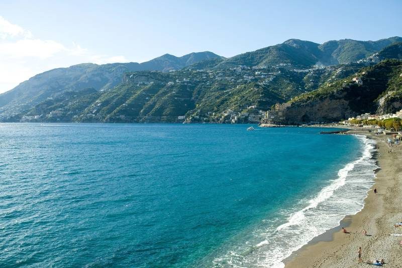 Plage avec sable, mer bleue et collines.