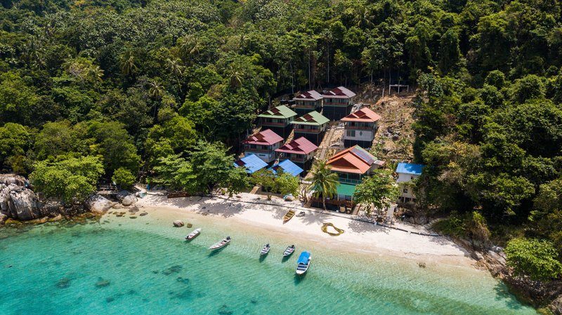 Vue aérienne de la plage de Coral Bay aux îles Perhentian, bordée de jungle tropicale et de bungalows colorés.
