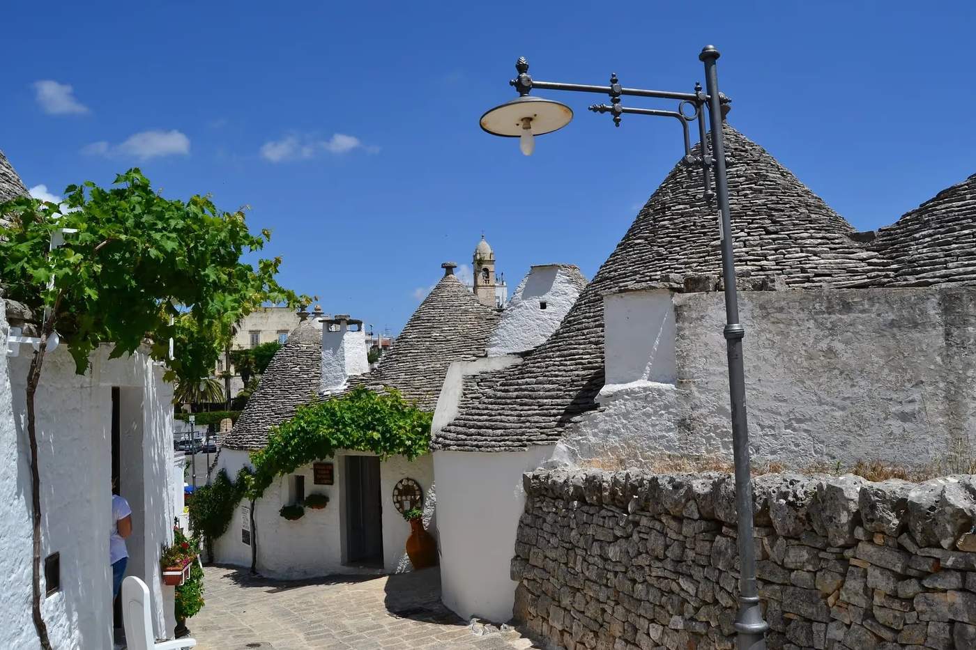 Rue pittoresque d'Alberobello avec des trulli traditionnels et un lampadaire vintage sous un ciel bleu.