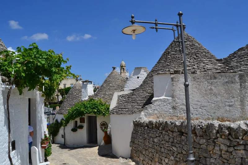 Rue pittoresque d'Alberobello avec des trulli traditionnels et un lampadaire vintage sous un ciel bleu.