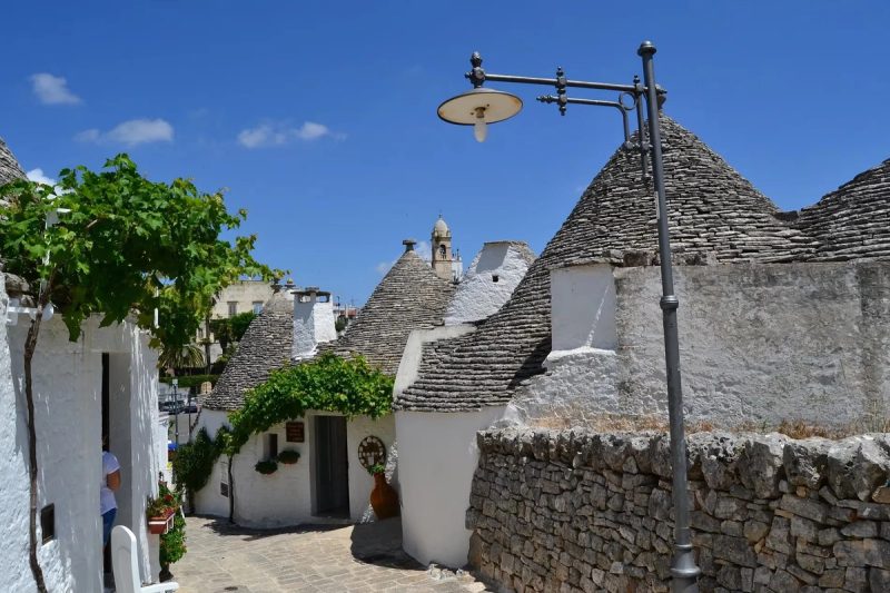 Rue pittoresque d'Alberobello avec des trulli traditionnels et un lampadaire vintage sous un ciel bleu.
