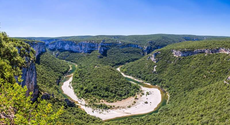 Vue panoramique sur les gorges de l'Ardèche depuis le belvédère, avec le méandre de la rivière entouré de falaises calcaires et de forêts verdoyantes