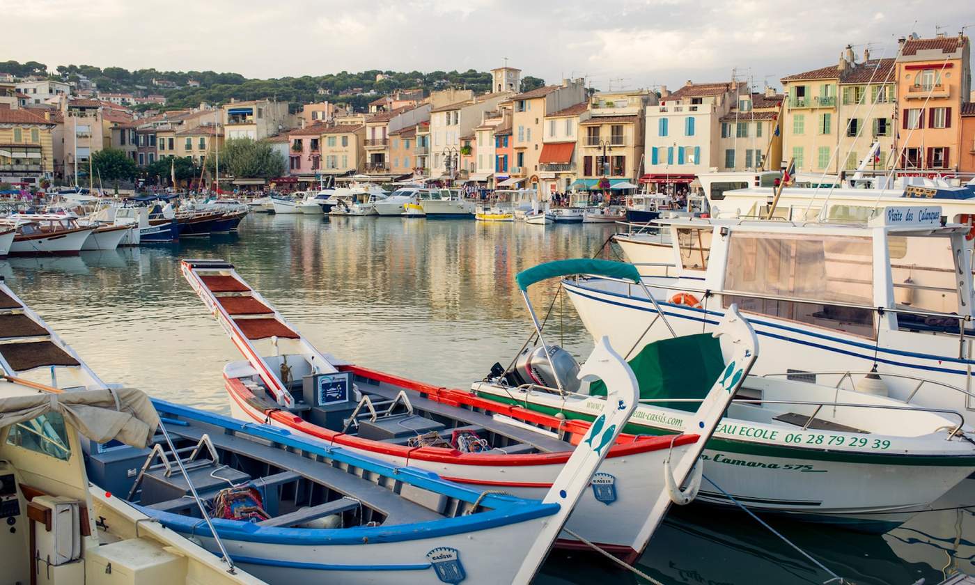 Barques traditionnelles et bateaux de plaisance amarrés dans le port de Cassis, avec en arrière-plan les façades colorées et les collines verdoyantes