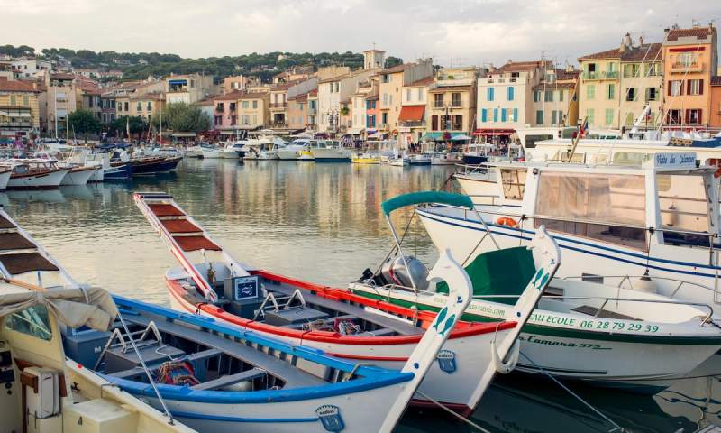 Barques traditionnelles et bateaux de plaisance amarrés dans le port de Cassis, avec en arrière-plan les façades colorées et les collines verdoyantes