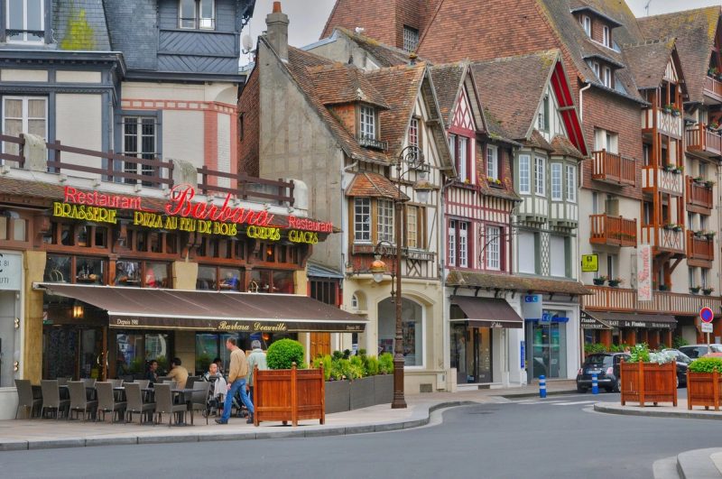 Façades à colombages colorées et terrasse de restaurant à Deauville, typiques de l’architecture normande.
