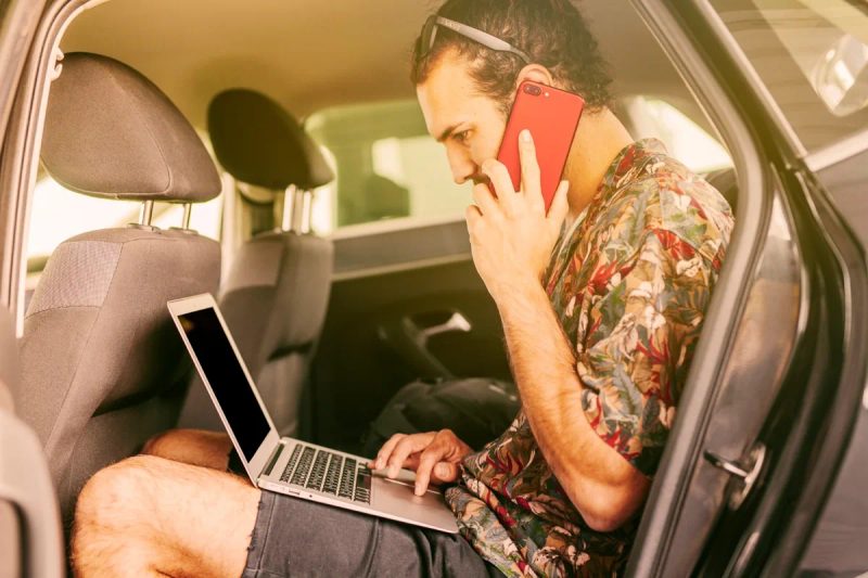 Homme travaillant sur un ordinateur portable dans une voiture tout en téléphonant