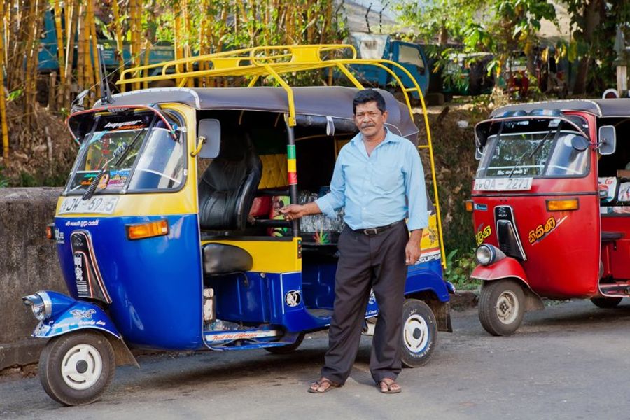 Conducteur de tuk-tuk à Kandy, Sri Lanka, posant à côté de son véhicule coloré prêt à transporter des passagers.