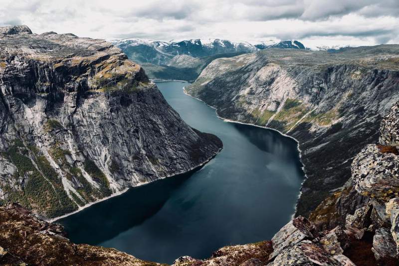 Vue panoramique d'un fjord majestueux en Norvège, entouré de montagnes escarpées et de l'eau calme.