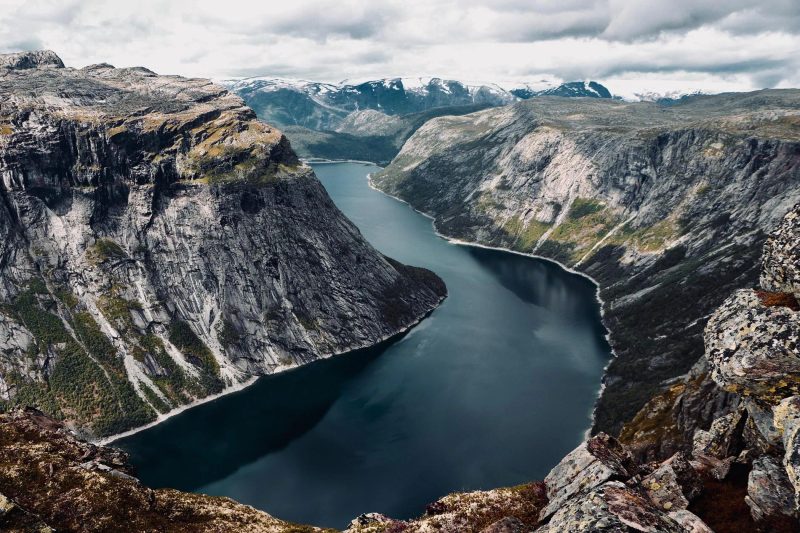 Vue panoramique d'un fjord majestueux en Norvège, entouré de montagnes escarpées et de l'eau calme.