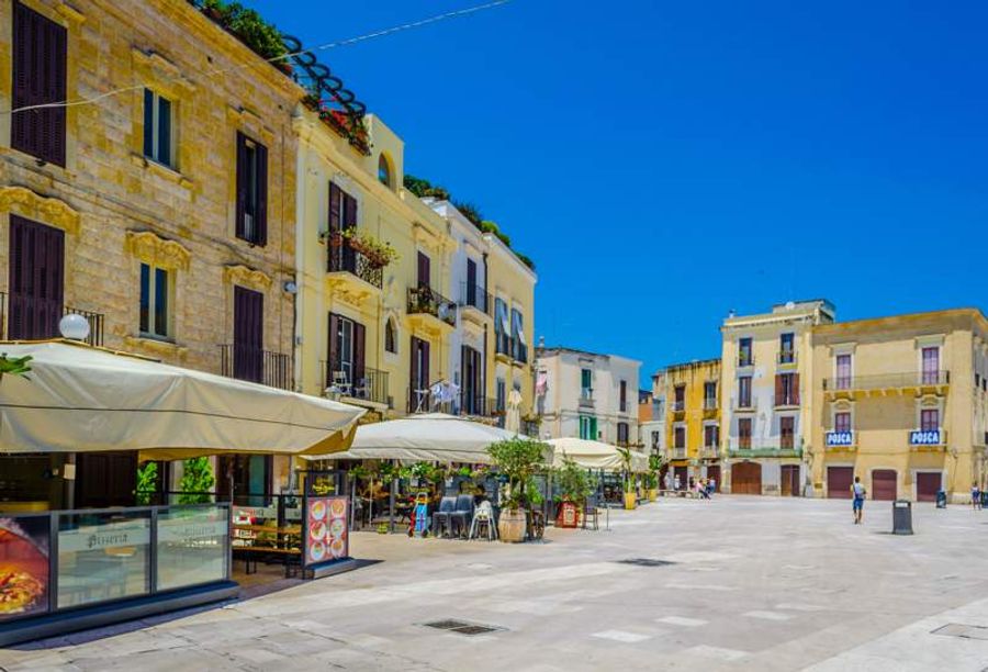 Vue animée de la Piazza Mercantile à Bari, bordée de bâtiments colorés et de terrasses accueillantes.