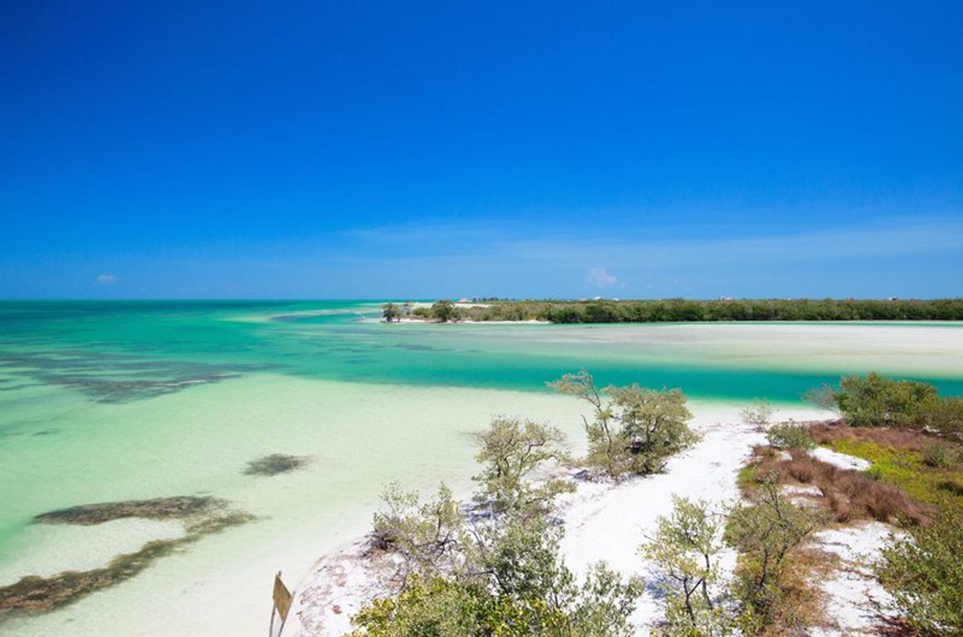 Vue panoramique de l'île d'Holbox avec ses plages de sable blanc et ses eaux turquoise, sous un ciel bleu.