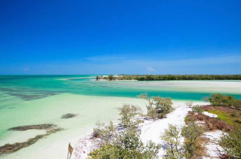 Vue panoramique de l'île d'Holbox avec ses plages de sable blanc et ses eaux turquoise, sous un ciel bleu.