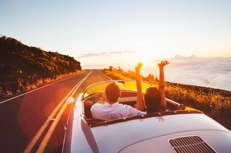 Un homme et une femme dans une décapotable longeant la mer au coucher du soleil