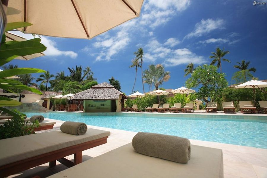 Piscine dans un resort en bord de mer, entourée de chaises longues et de parasols, sous un ciel bleu clair.