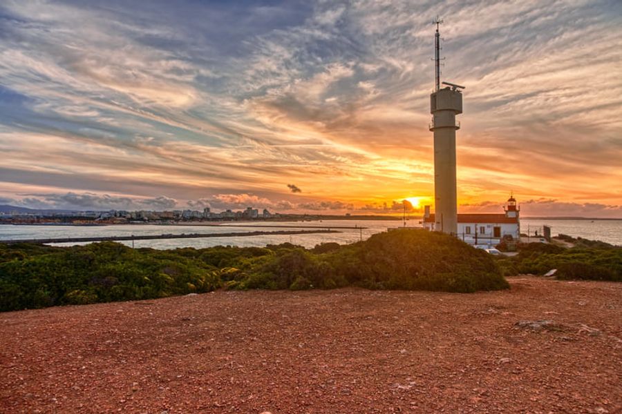 Un phare moderne surplombant la mer avec une vue spectaculaire du coucher de soleil, entouré de végétation et d
