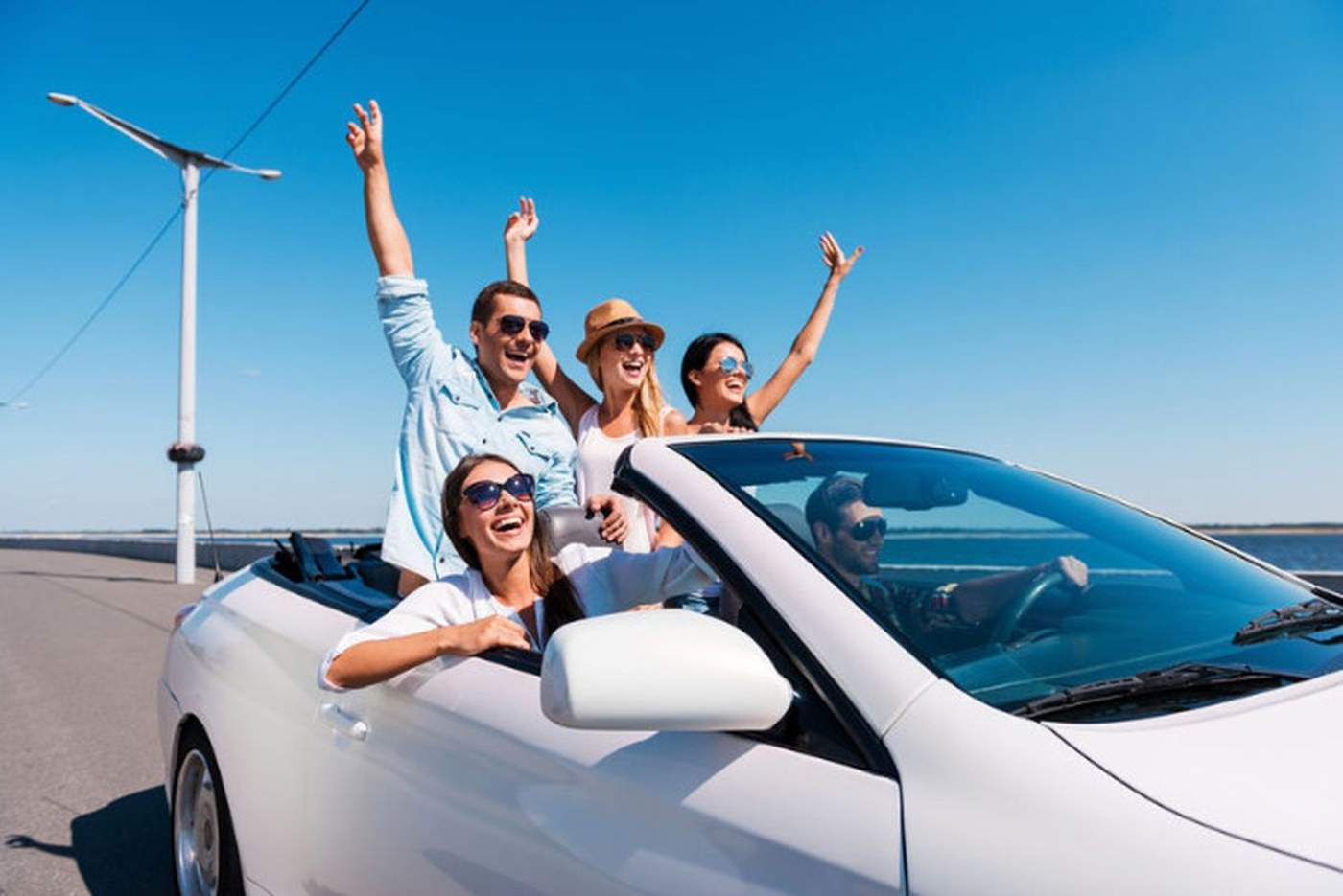 Groupe d'amis heureux en road trip dans une voiture décapotable blanche, bras levés au soleil
