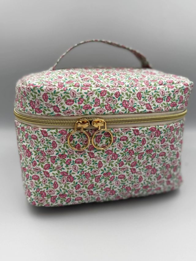 A quilted pink floral vanity case with a handle and a gold zip with two ring pulls
