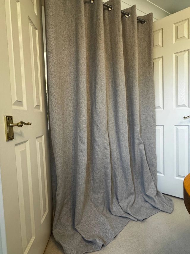 Long grey curtain pooling on a beige carpet, before