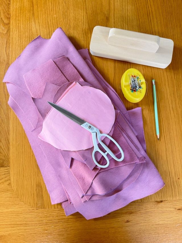 Lilac fabric with pink pattern pieces, scissors, a pincushion and a chalk pencil on a wooden table
