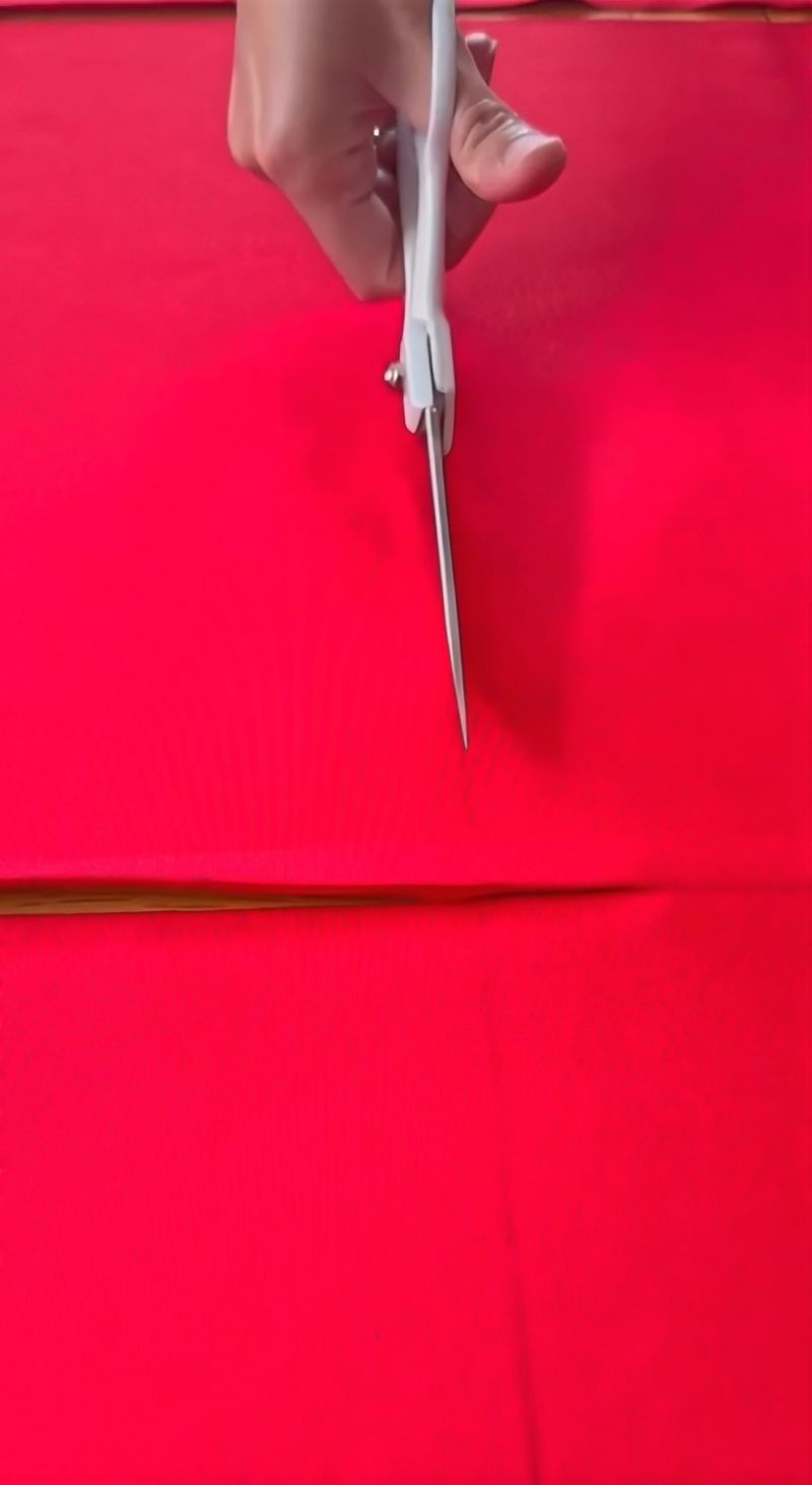 Shears cutting a straight line through red fabric on the cutting table