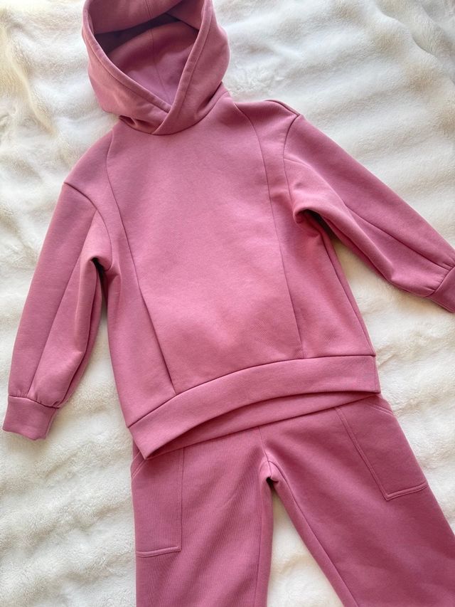 Child's dusty pink hoodie and jogger set laid flat on a white rug