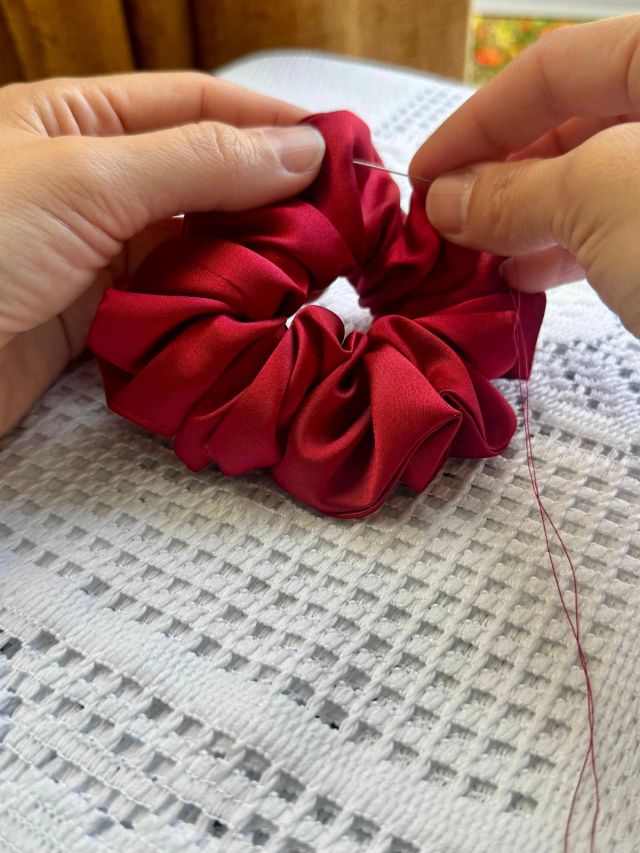 Closing a red satin scrunchie by hand with a needle and matching red thread