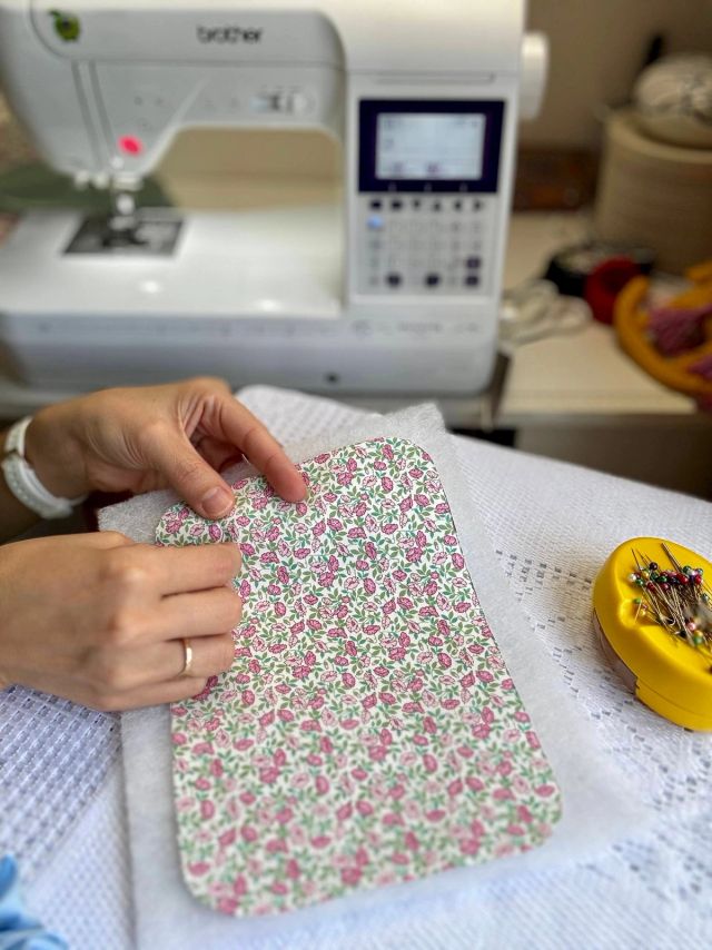 Smoothing a rounded piece of pink-and-green floral cotton onto white wadding, a yellow pincushion beside it