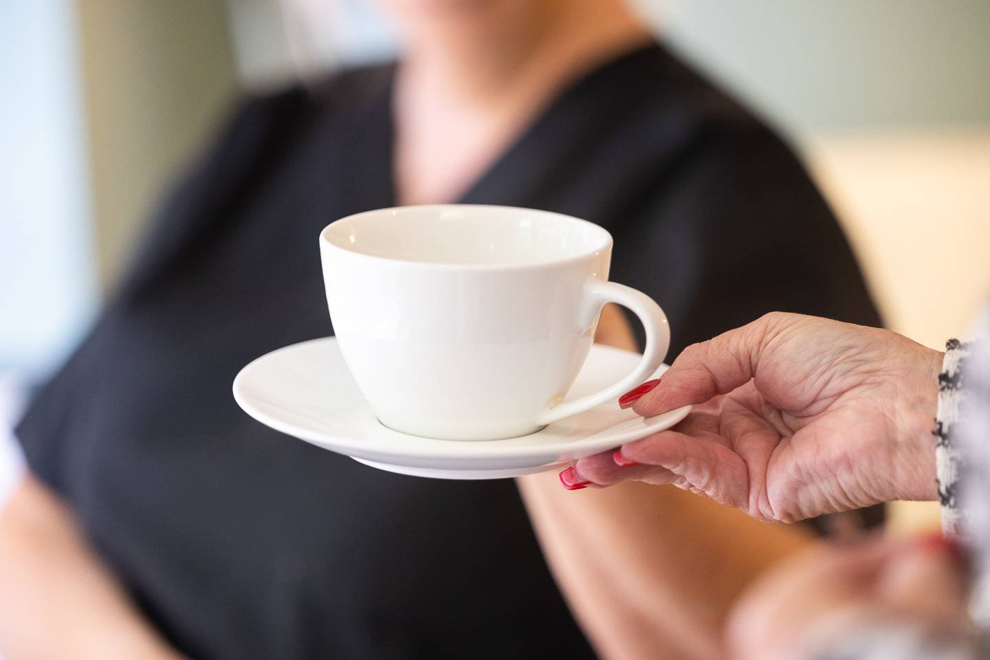 White tea cup and saucer being handed to patient's hand from dental nurse