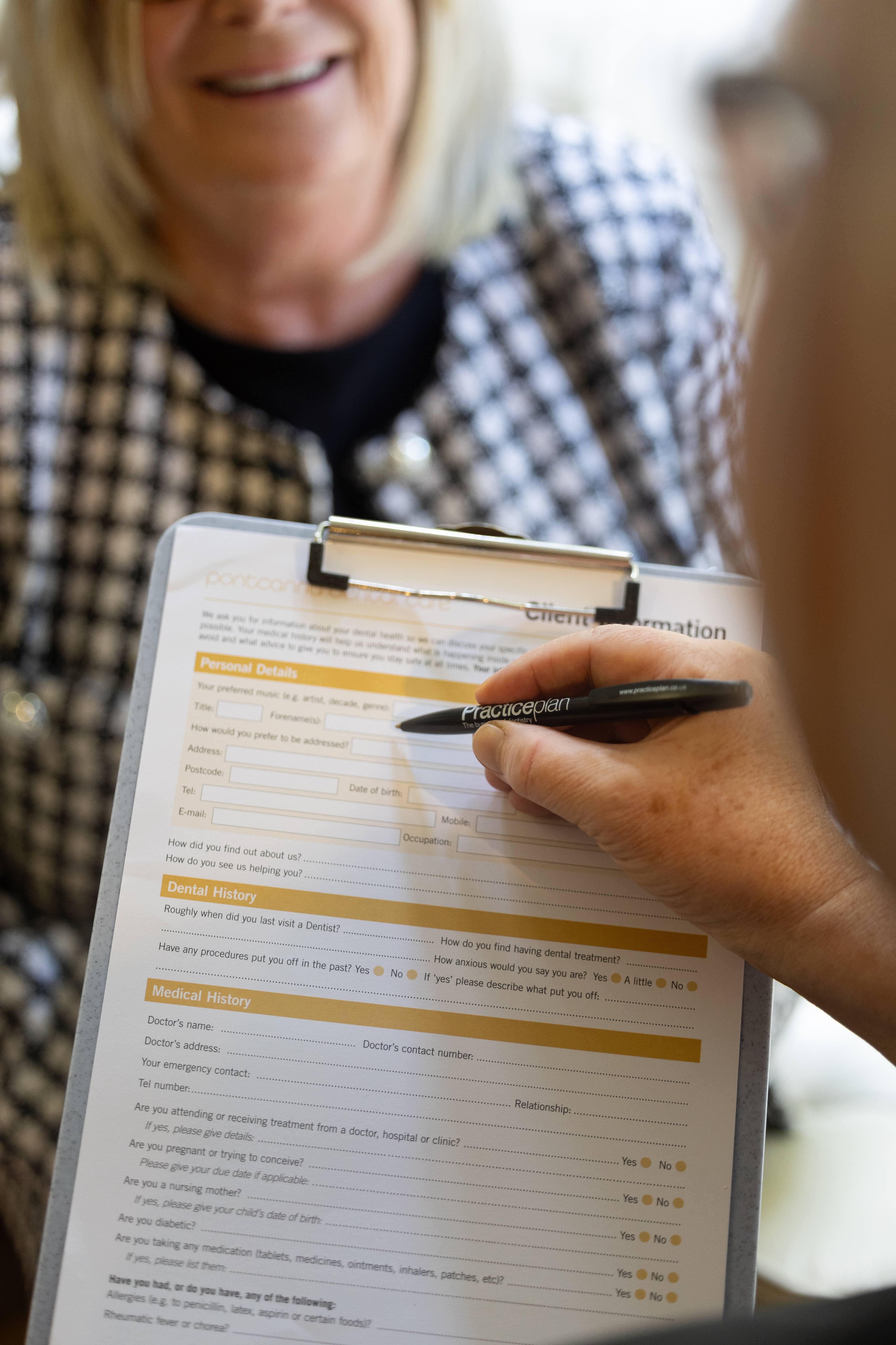 Female receptionist talking through a patient details form with a patient holding pen