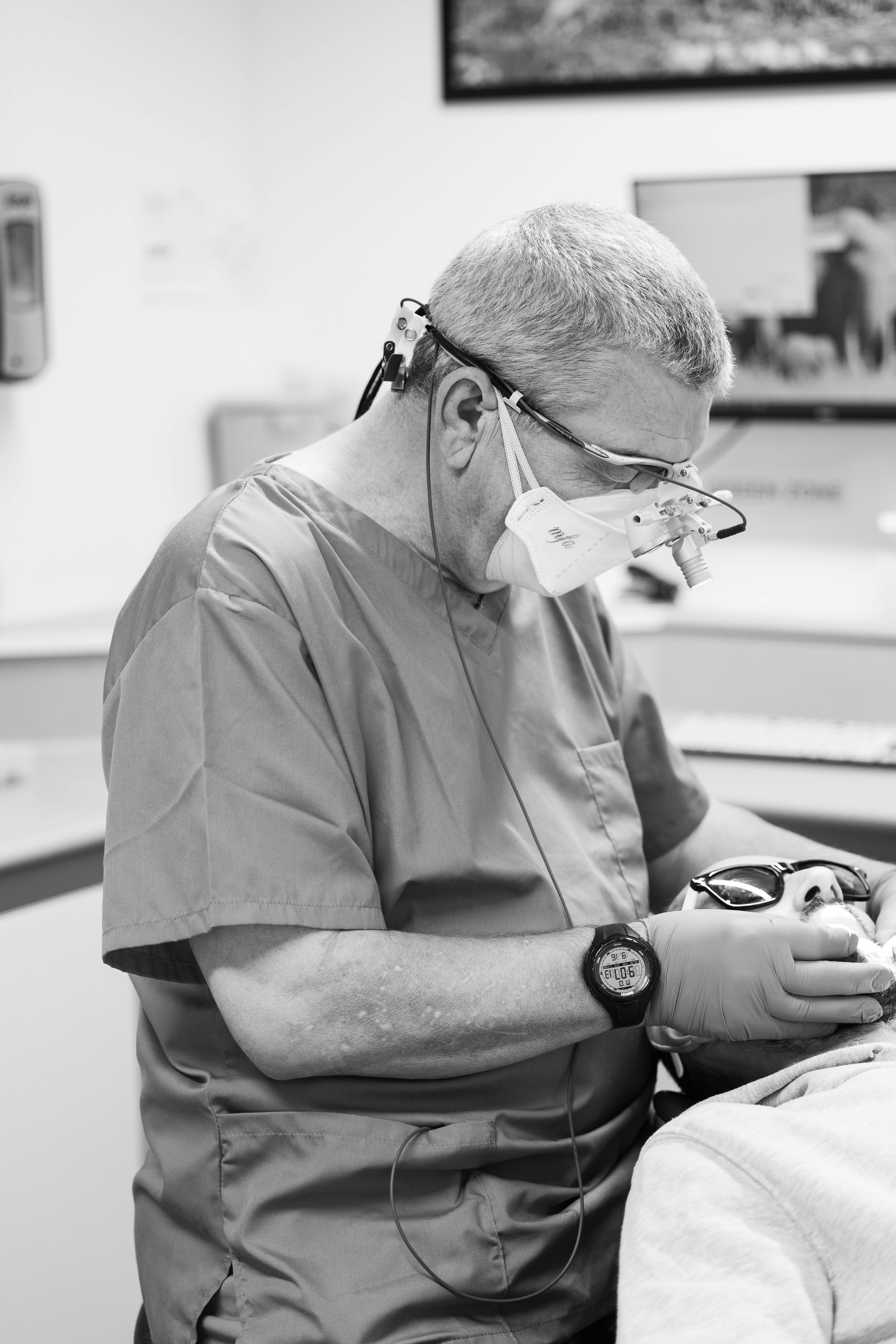 Black and white photograph of Pontcanna male dentist wearing loupes treating male patient 