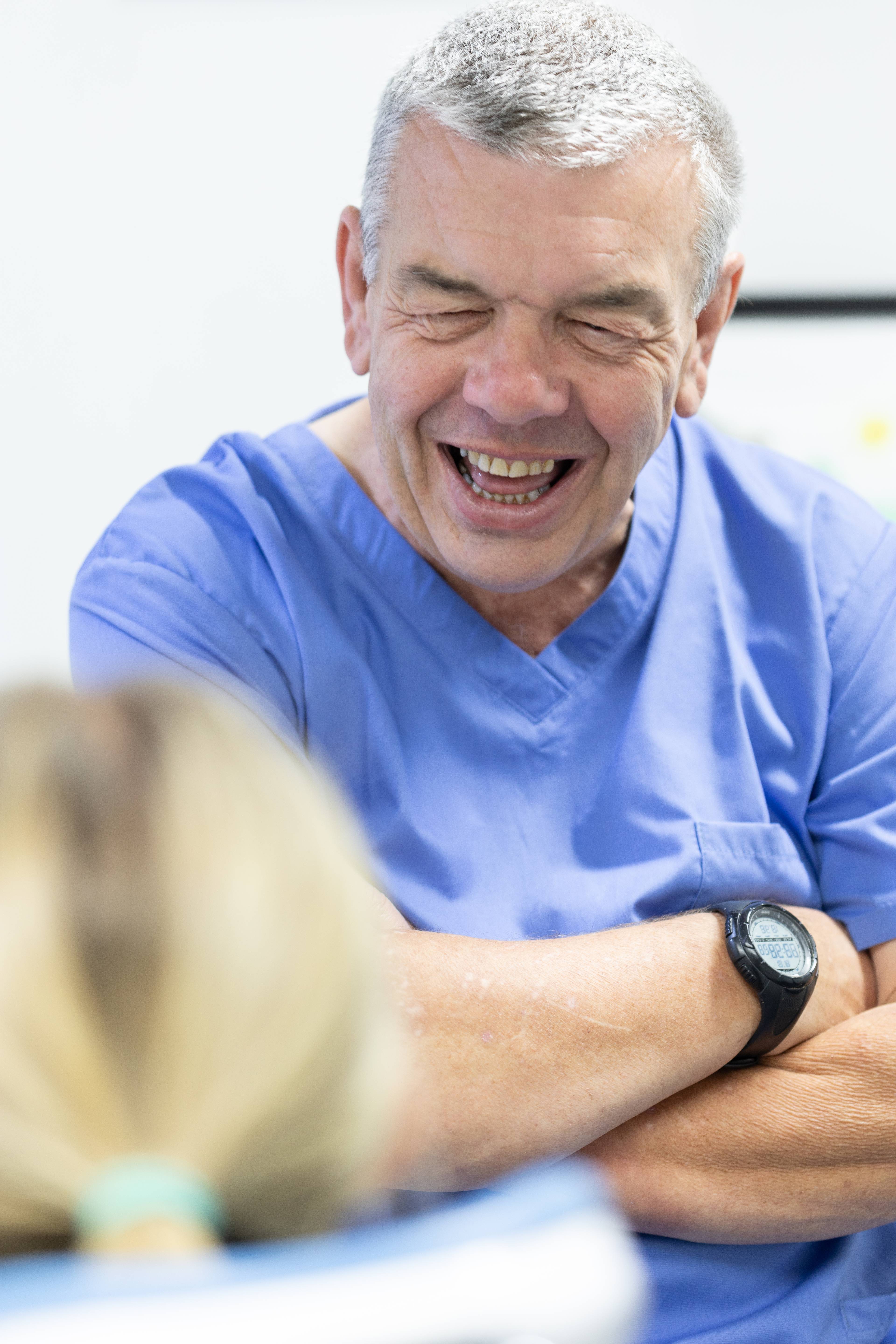 male dentist in blue uniform laughing with patient during consultation