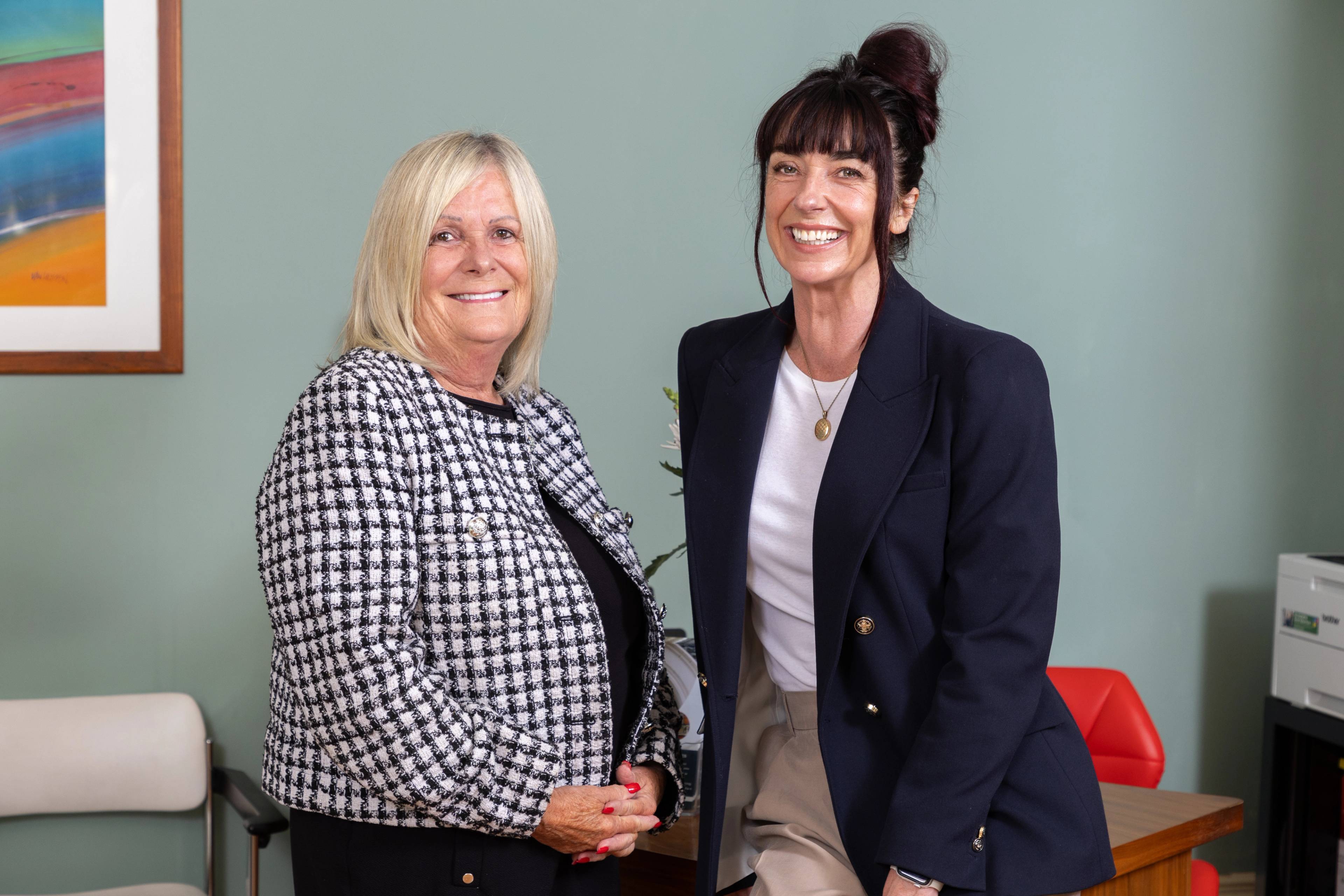 two smiling receptionists sitting at the edge of the desk welcoming patients