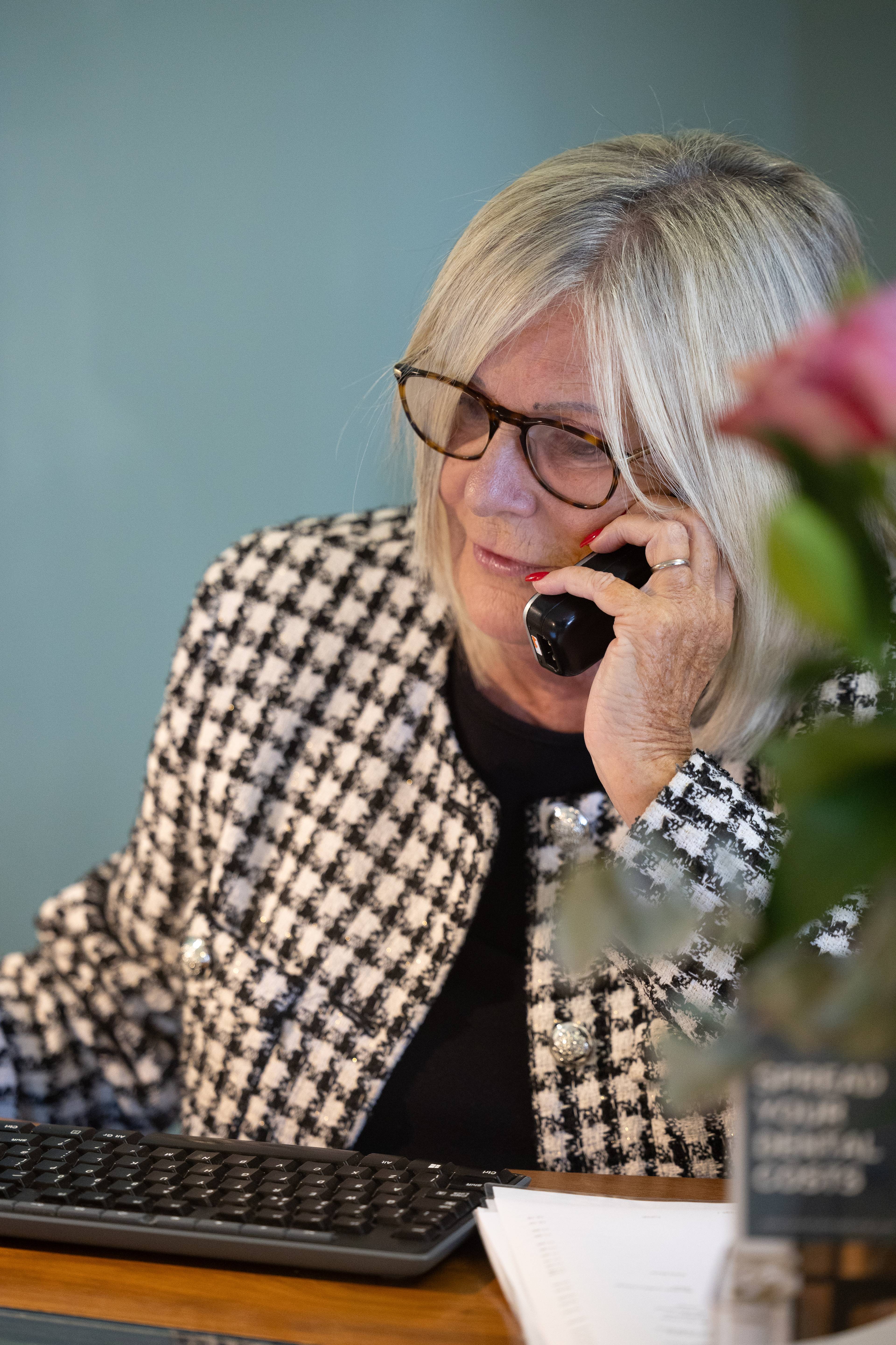 Female receptionist sat at her desk on the phone to a patient with pink flowers in foreground