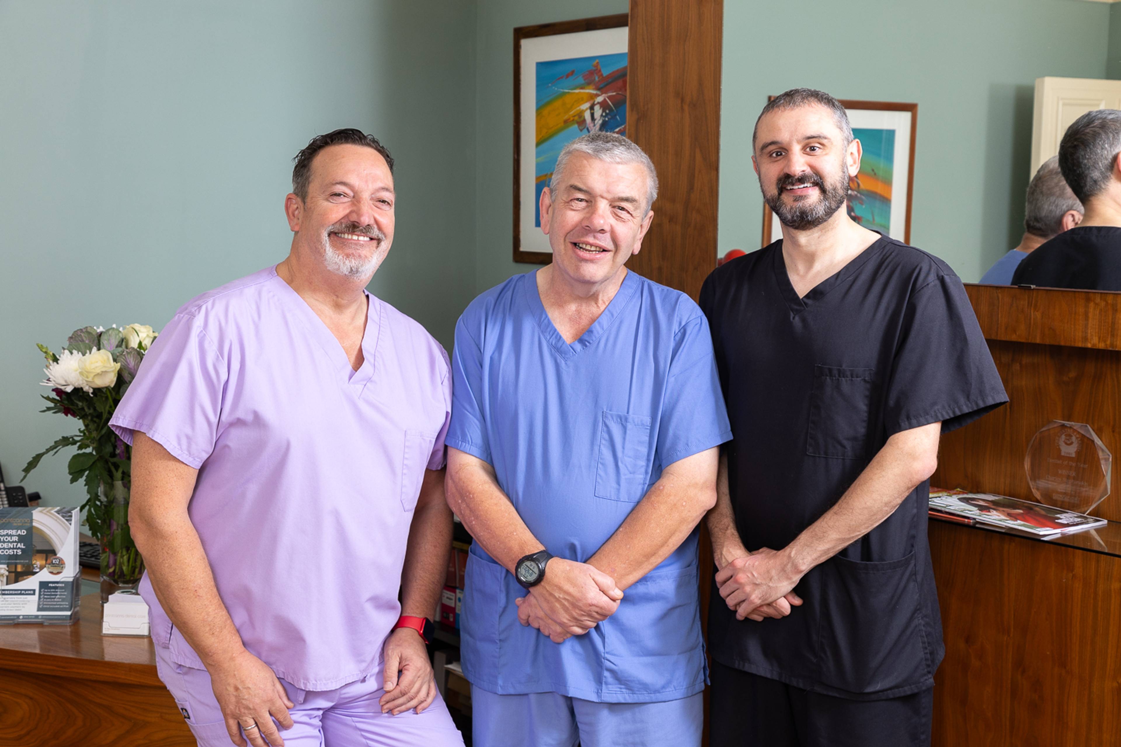 Three dentists at Pontcanna Dental Care smiling together in a beautiful, calm reception area