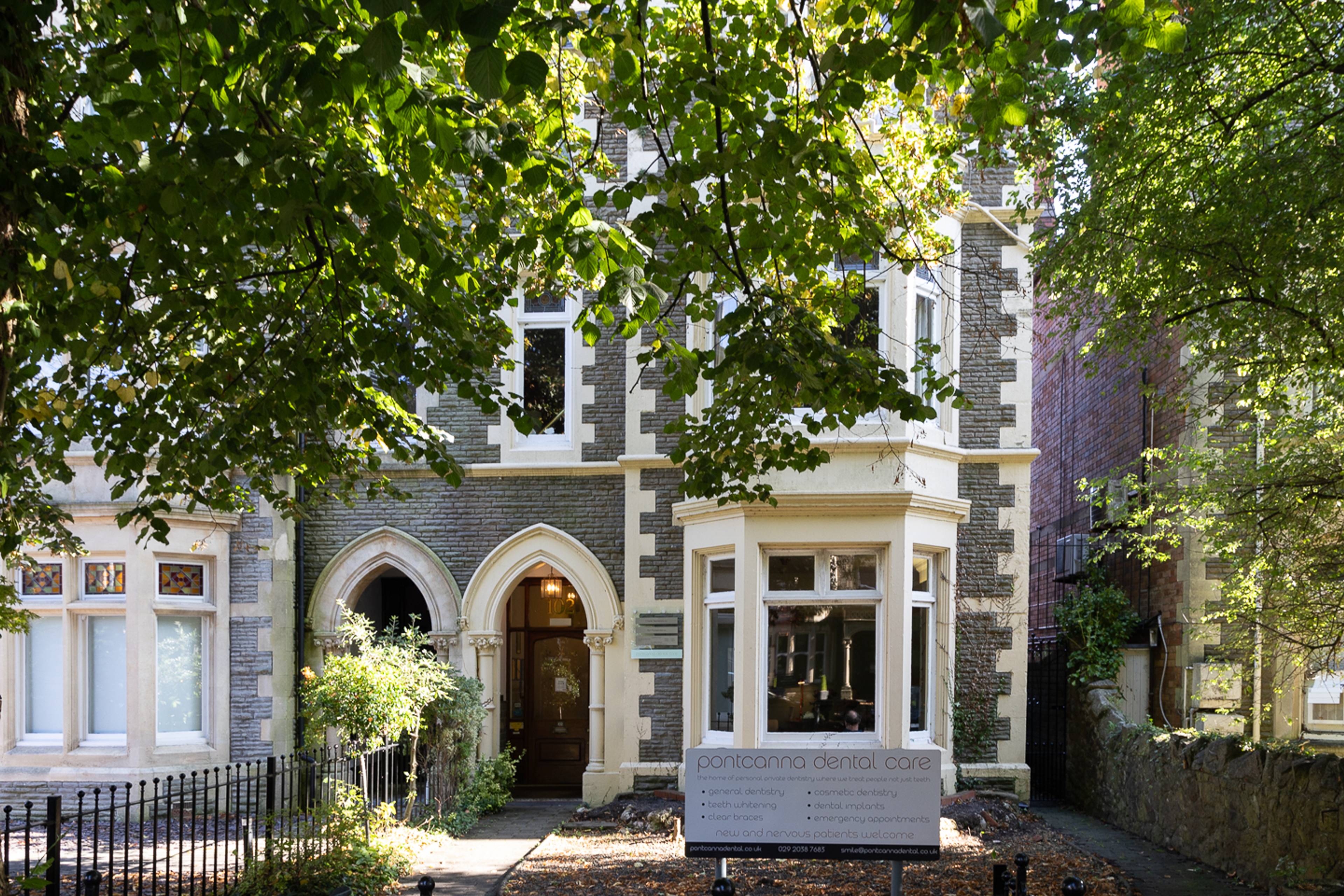 Outside front garden at Pontcanna Dental Care featuring pathway towards arch door, bay window and large tree 