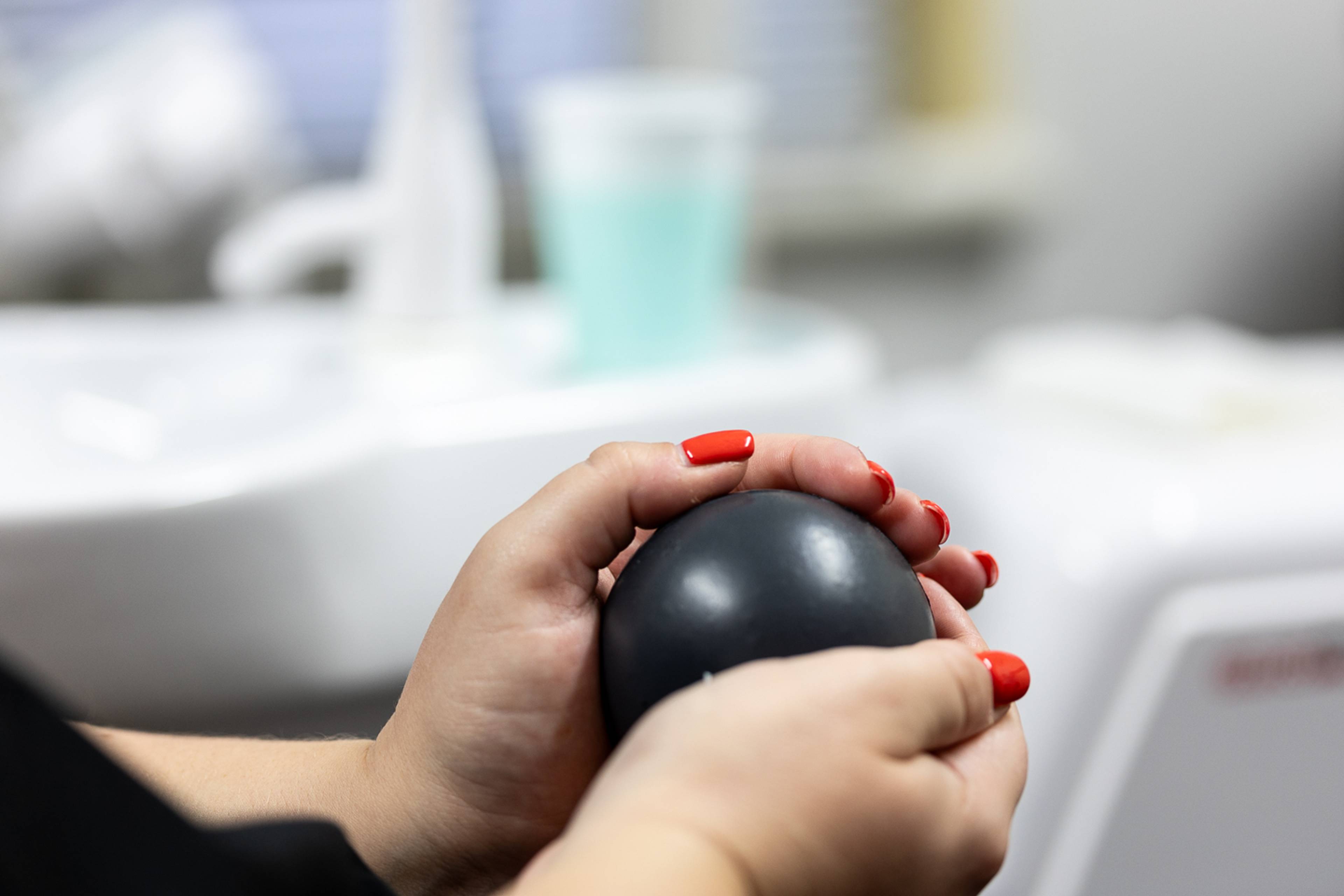 close up of female with red painted nails holding stress ball 