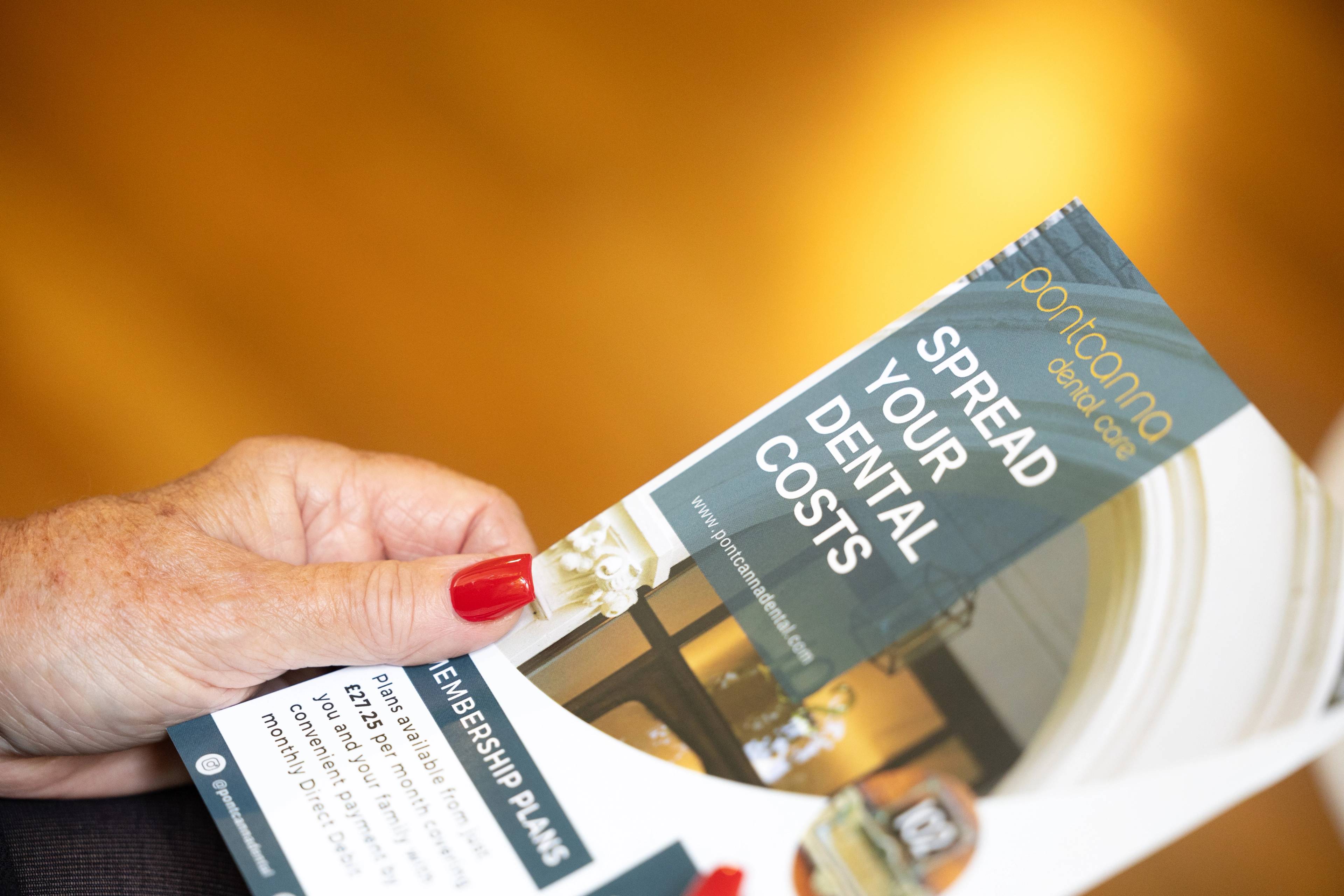 female patient with red nails holding information leaflet against gold background about spreading dental costs