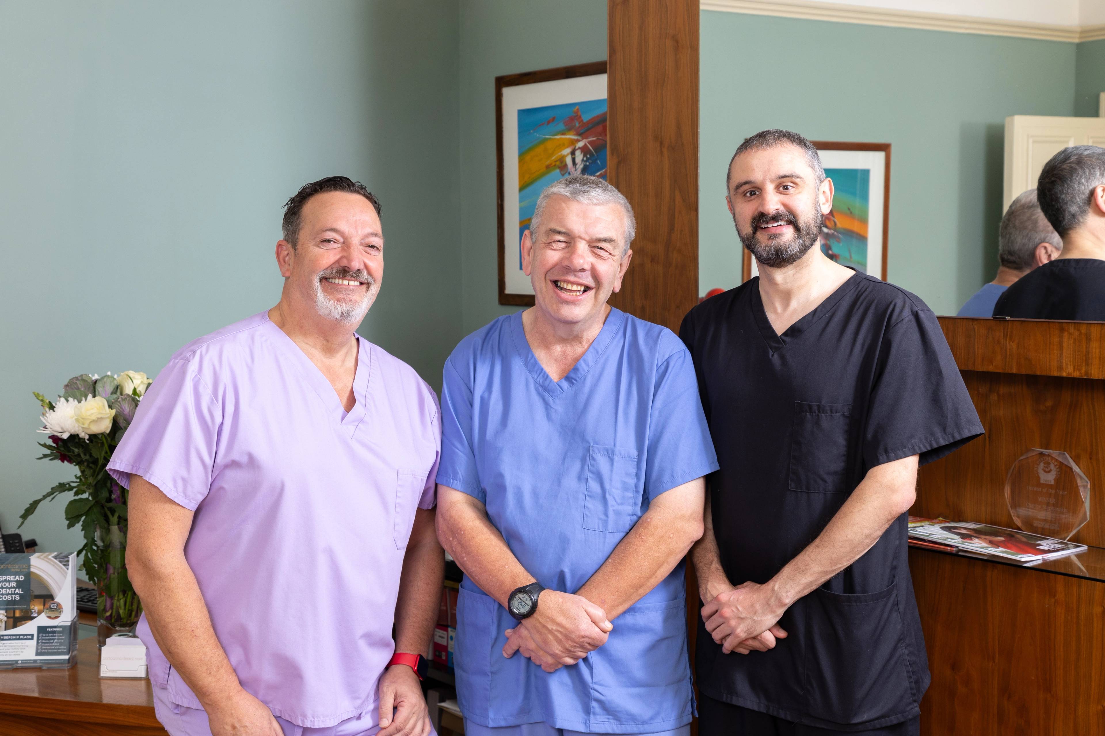 three male dentists in uniform standing and smiling in brightly coloured waiting room