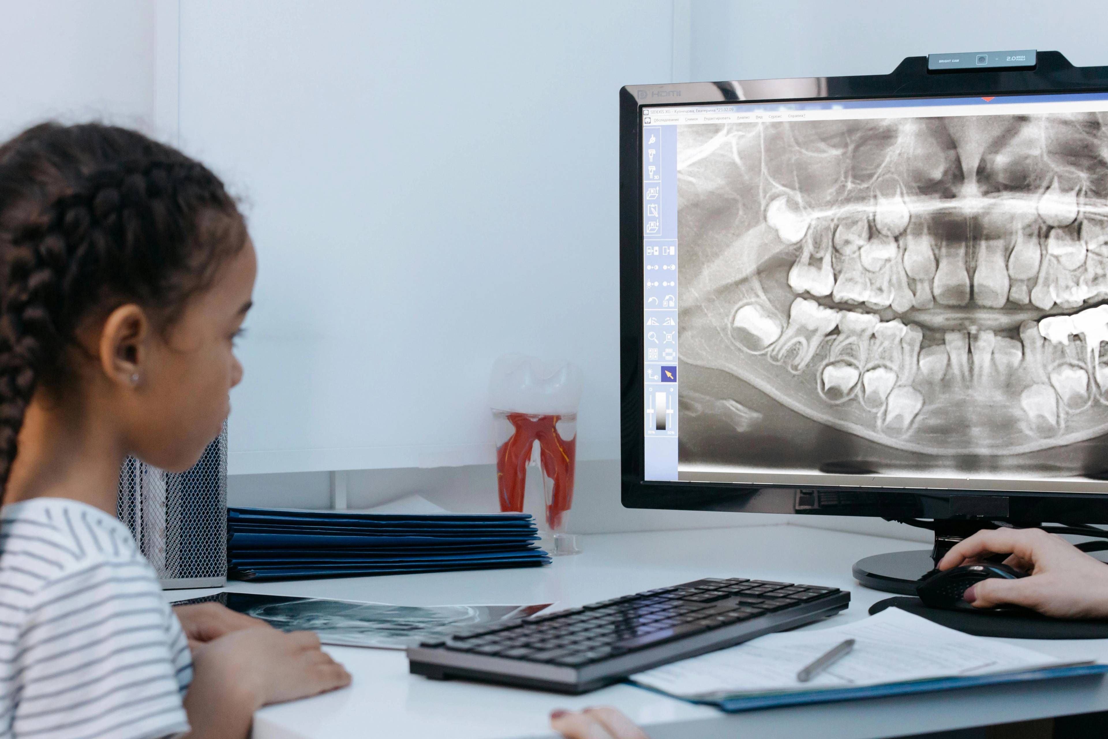 female child patient sat in dentists surgery looking at x-ray on computer screen
