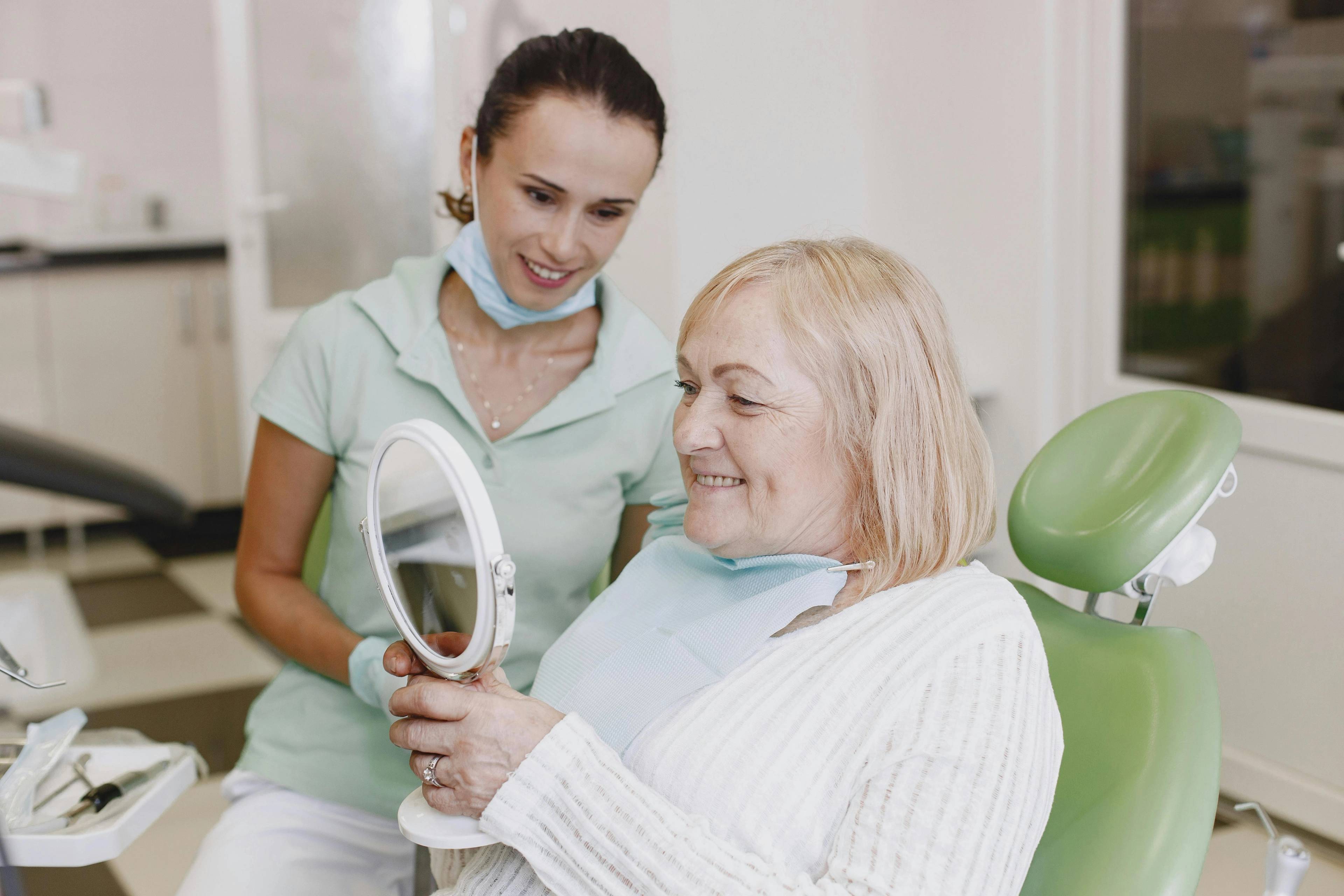 female patient smiling as female dentist holds a handheld mirror, patient is pleased with new implants