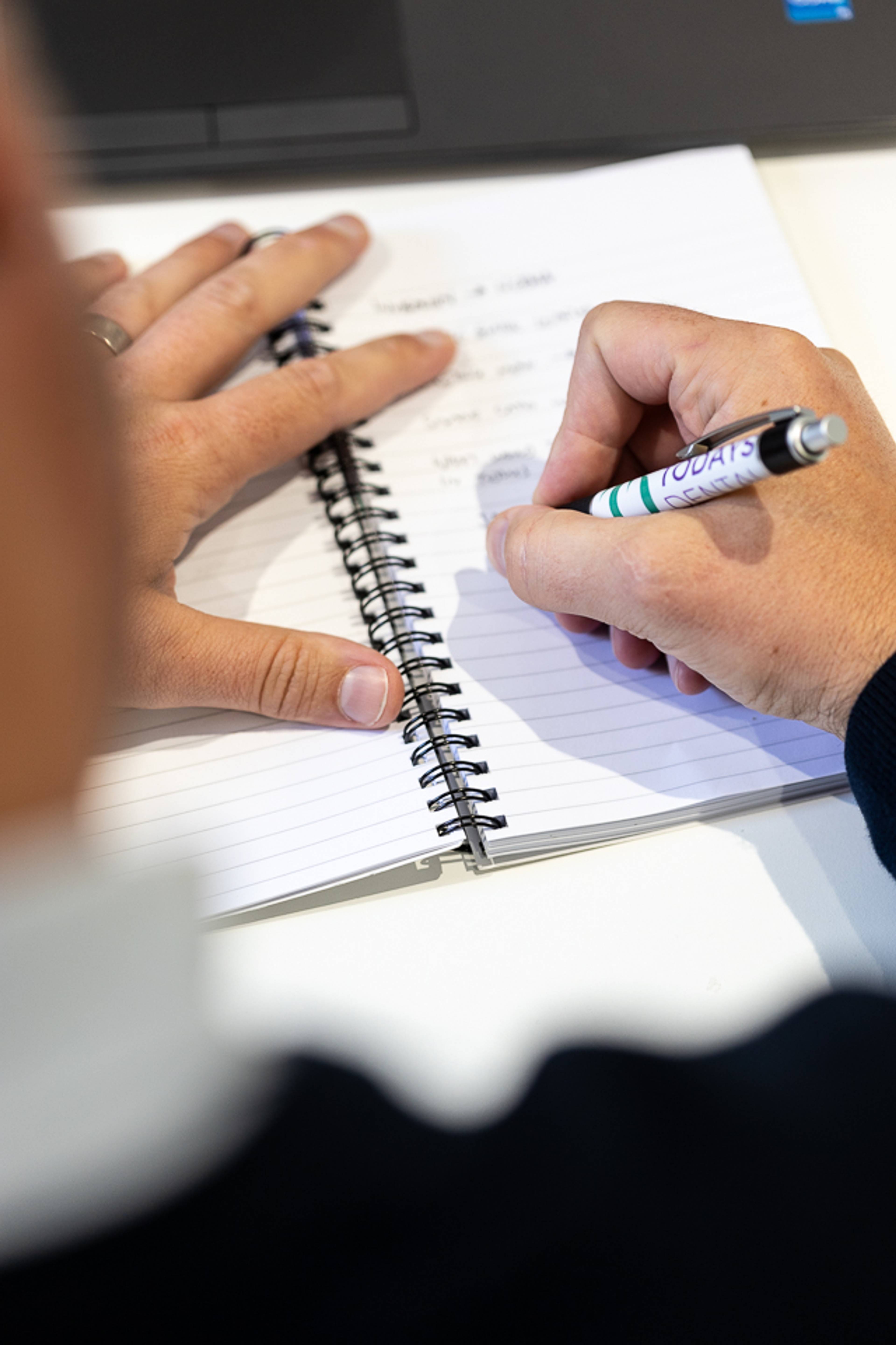 close up of person holding pen and writing in notepad